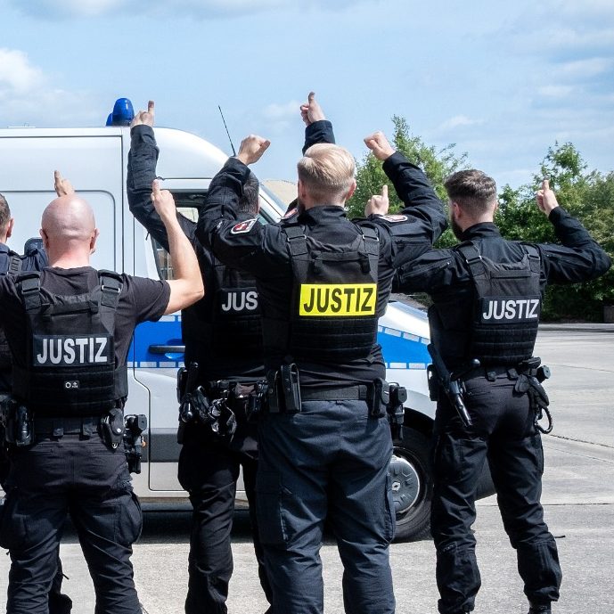 Polizisten zeigen mit Daumen nach oben, vor einem Einsatzfahrzeug.